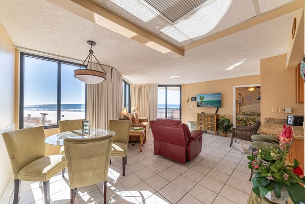 A spacious living room with a view of the beach, a dining area with a round table, and a red reclining chair. - Surfside Sandcastle-Sunbird-Beachfront PCB, King Suite-Book Summer Vacay Now! (Panama City Beach)