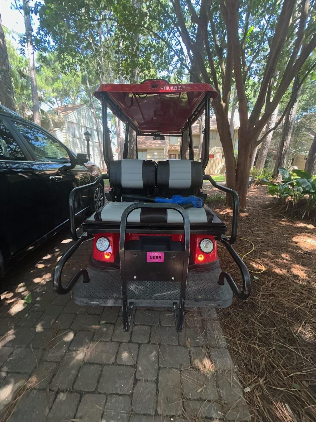 Un carrito de golf estacionado en un camino pavimentado con árboles al fondo.