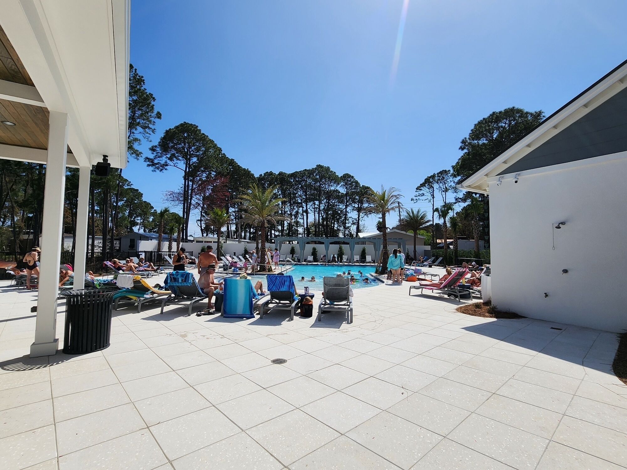 A pool area with lounge chairs and umbrellas, surrounded by trees and a covered seating area.