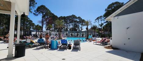 A pool area with lounge chairs and umbrellas, surrounded by trees and a covered seating area.