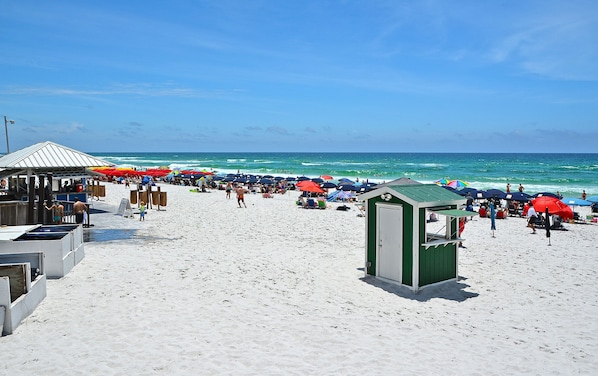 A beach with a green lifeguard station, umbrellas, and beachgoers.