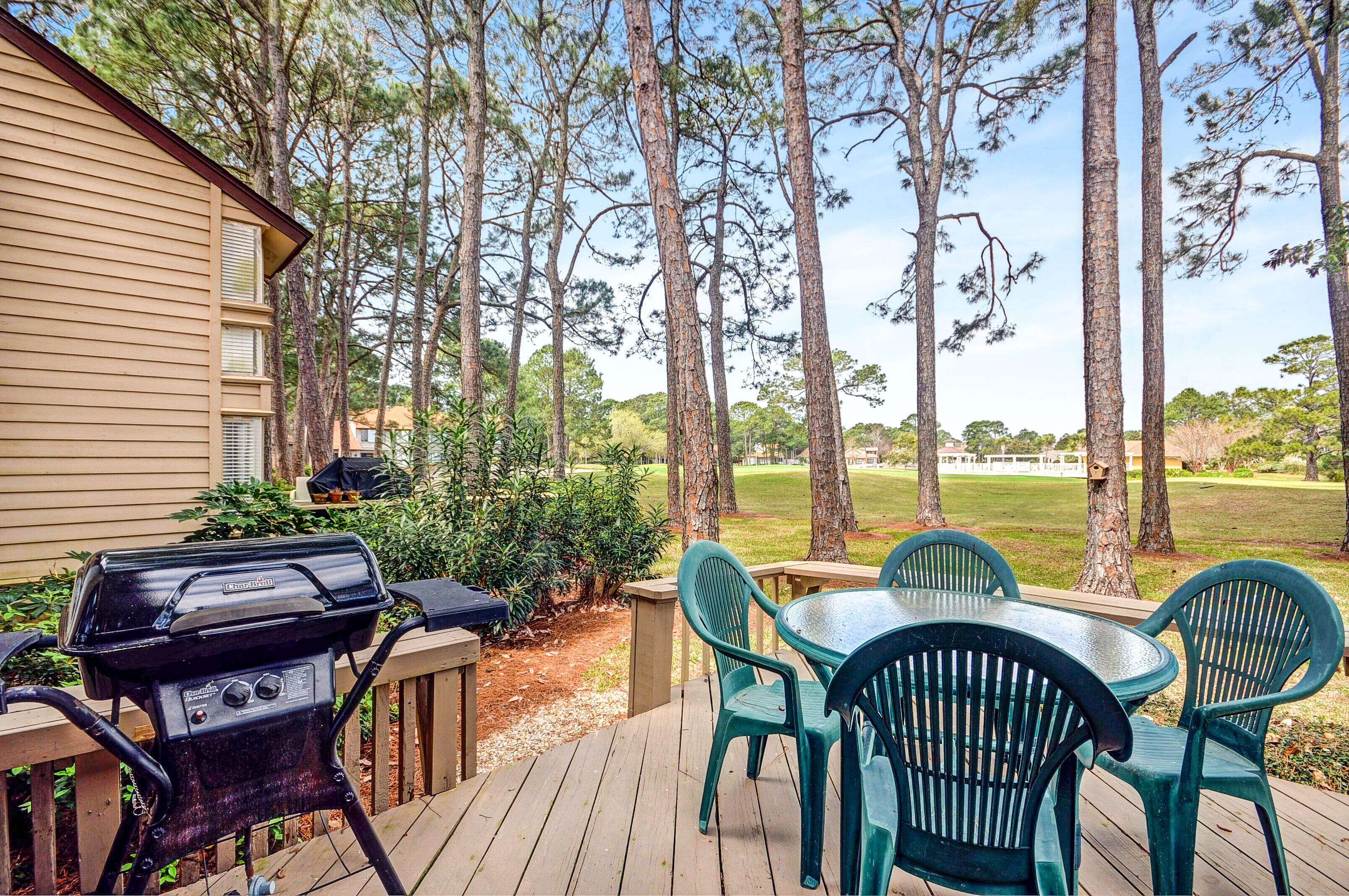 A deck with a grill, chairs, and a view of a golf course.