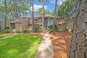 A two-story residential building with a front yard, a pathway leading to the entrance, and a small fenced area.