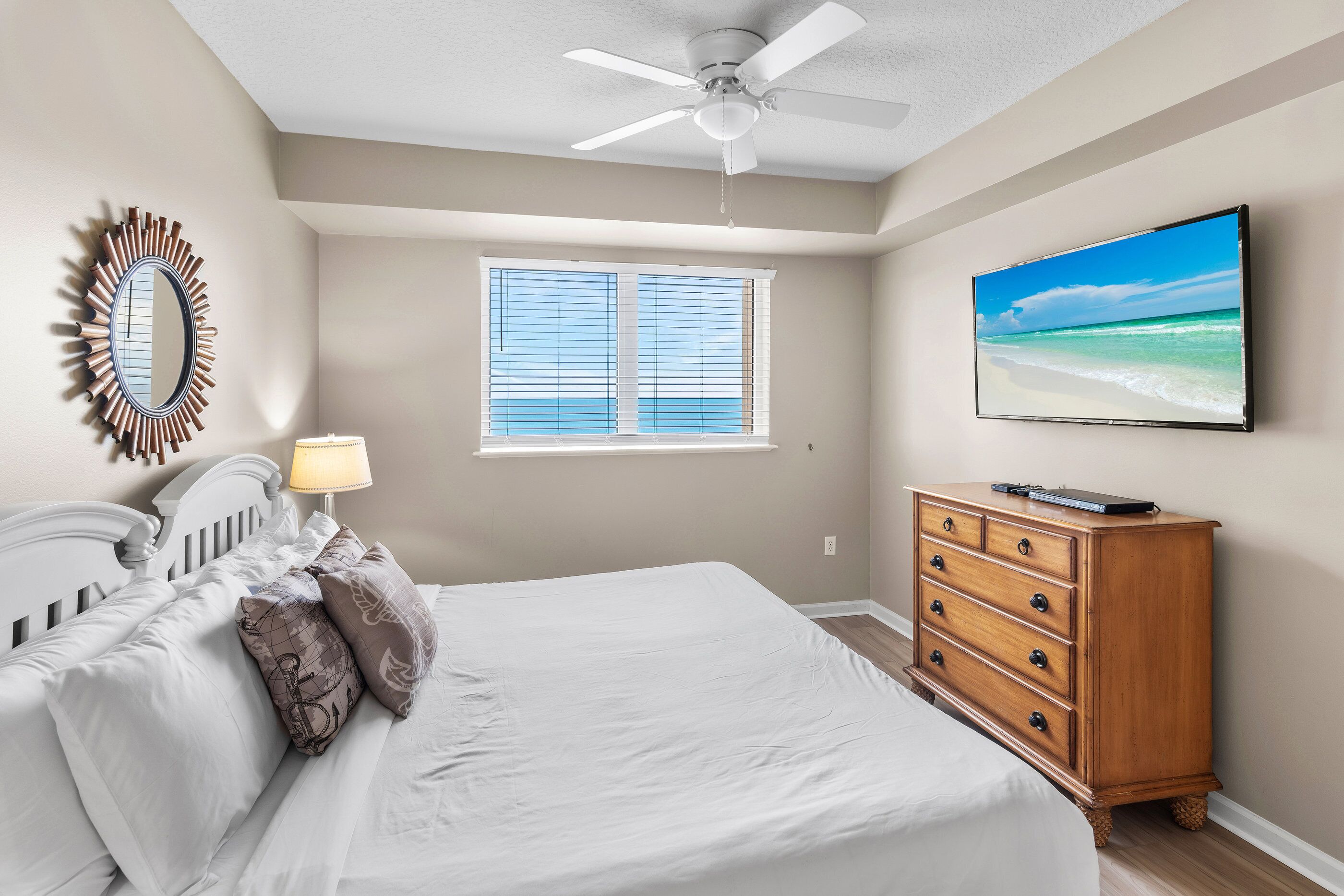 Een slaapkamer met een bed, een dressoir, een plafondventilator, een raam met zonwering en een televisie aan de muur.