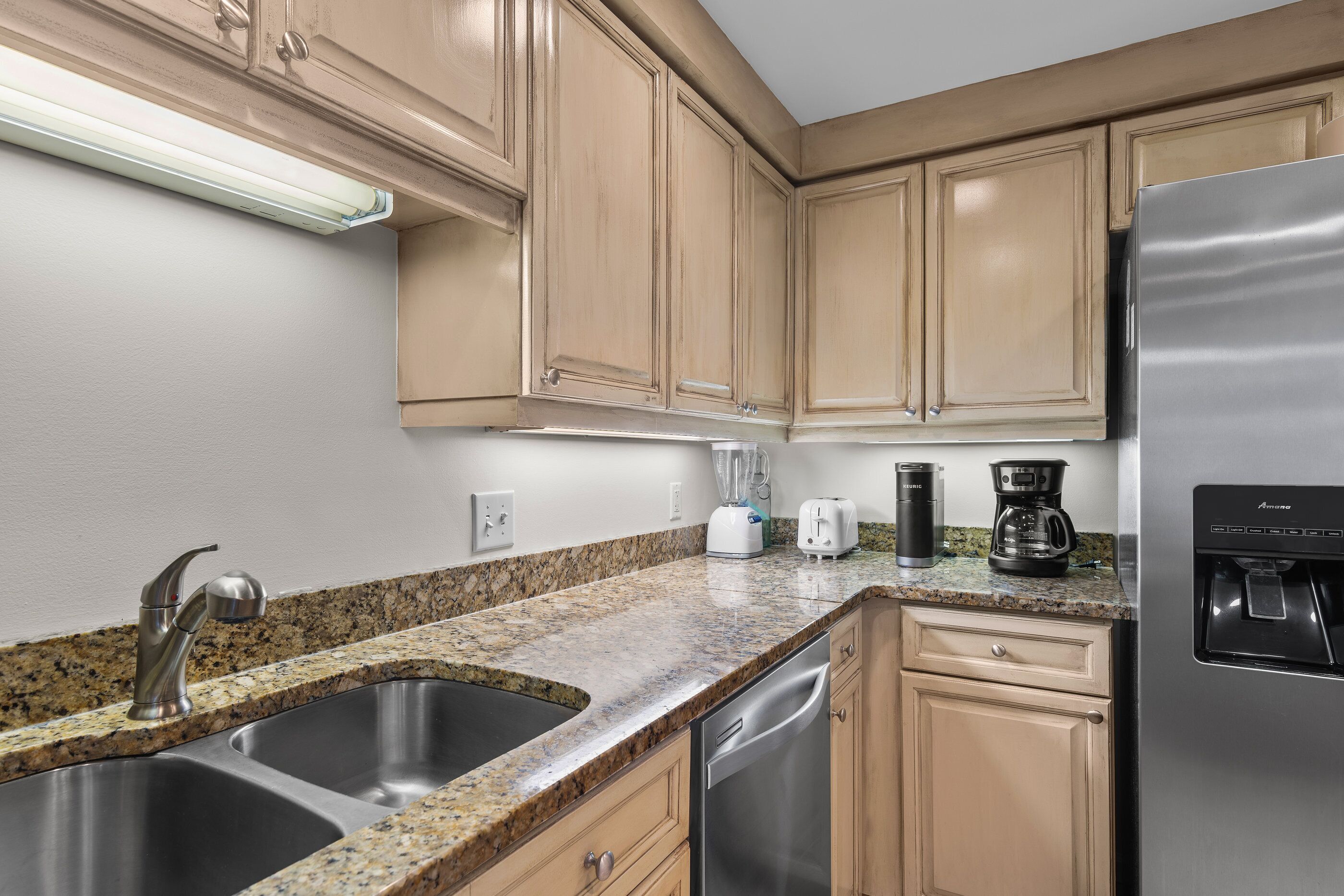 A kitchen with stainless steel appliances, granite countertops, and beige cabinetry.