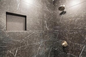 A shower area with a marble wall, a circular drain, and a recessed control panel.