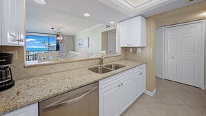 A modern kitchen with white cabinetry, granite countertops, and a large window overlooking a scenic view.