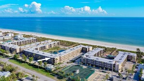 A beachfront hotel with multiple buildings, a tennis court, and a clear view of the ocean.