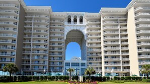 A multi-story hotel with a central archway, balconies, and a clear blue sky.