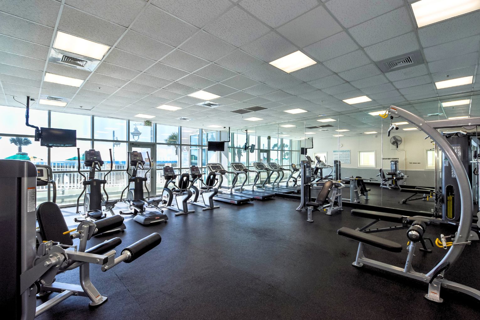 Une salle de sport équipée de machines de cardio, de matériel d’entraînement en force et d’un grand miroir.