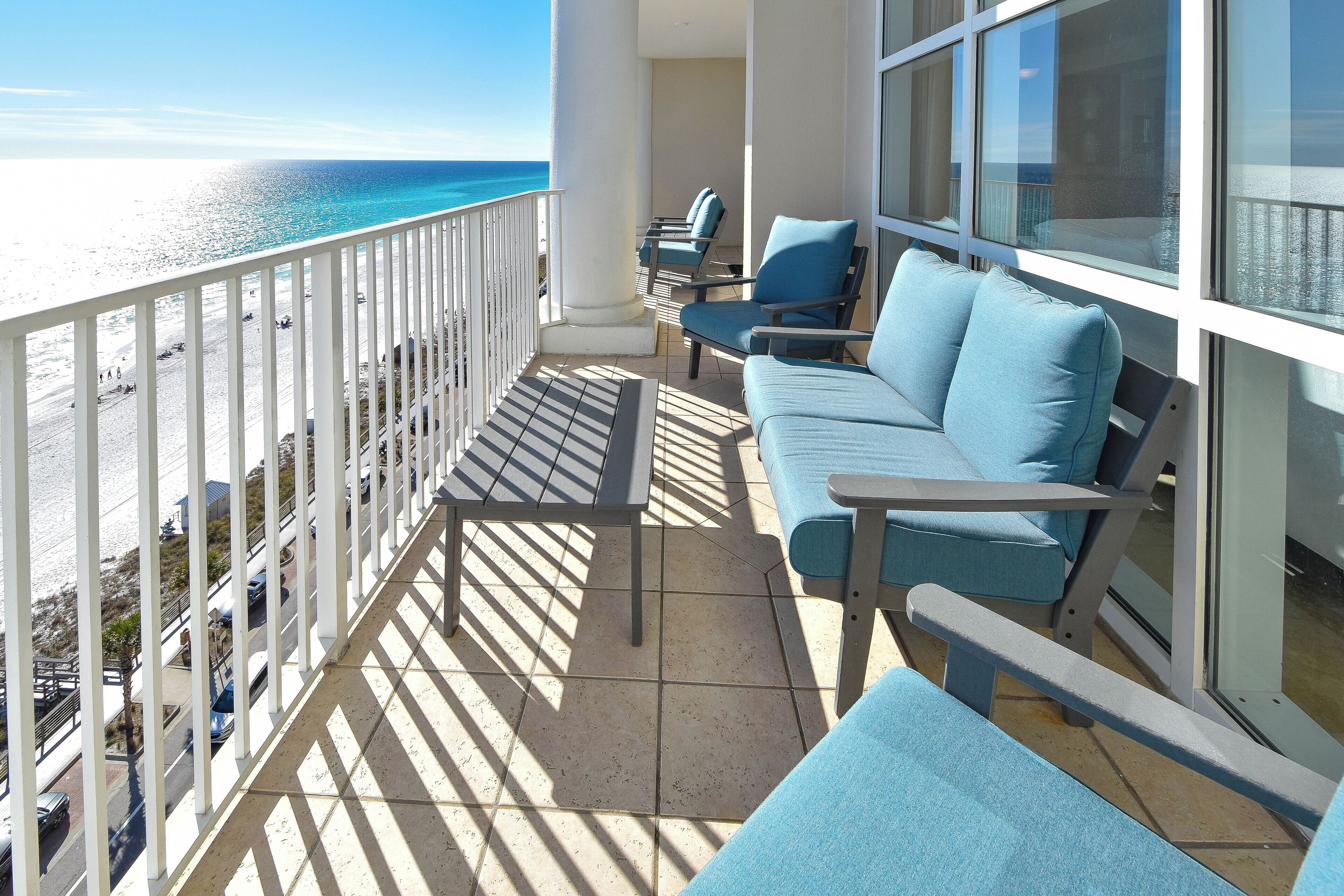 Un balcon avec vue sur la plage et l’océan, aménagé avec des chaises bleues et un canapé.