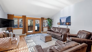 A spacious living room with leather sofas, a flat-screen TV, and a large window with curtains. - Downtown Gem - Ski Resort Views, Private Hot Tub, Dog-Friendly MainD (Breckenridge)