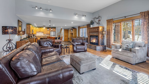 A spacious living room with a large leather sofa, a grey ottoman, and a fireplace. There is a dining area with wooden cabinets and a kitchen in the background. - Downtown Gem - Ski Resort Views, Private Hot Tub, Dog-Friendly MainD (Breckenridge)
