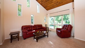 Un salon spacieux avec un plafond haut, un canapé en cuir rouge, un fauteuil assorti et une petite table.