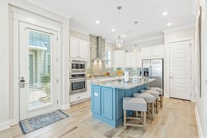 A modern kitchen with a central island, built-in appliances, and a light blue accent wall. - TipSea Kitty - 3BR/2.5BA Prominence Home - Sleeps 8 - 6-Seat LSV & Community Pool (Rosemary Beach)