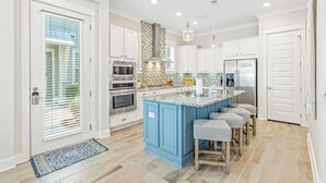 A modern kitchen with white cabinets, a blue island, stainless steel appliances, and a patterned backsplash. - Prominence on 30A - LSV Included - "Tipsea Kitty" - Virtual Tour (Rosemary Beach)
