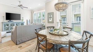 A dining area with a round table, chairs, a chandelier, and a television in the background. - Prominence on 30A - LSV Included - "Tipsea Kitty" - Virtual Tour (Rosemary Beach)
