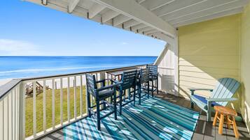 A covered deck with a view of the ocean, featuring a blue and white striped rug, a wooden chair, and a small stool.
