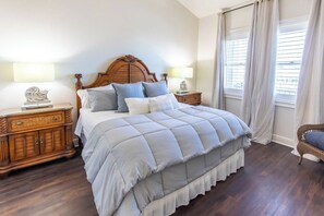 A bedroom with a large bed, wooden headboard, two bedside tables with lamps, a dresser, and a window with curtains.