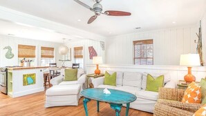 A spacious living room with a white sofa, a turquoise coffee table, and a ceiling fan. - Just Beachy | Pet Friendly, Pool, Fenced Yard! (Tybee Island)