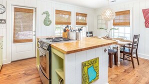 A kitchen with a wooden island, a stove, and a dining area with chairs. - Just Beachy | Pet Friendly, Pool, Fenced Yard! (Tybee Island)