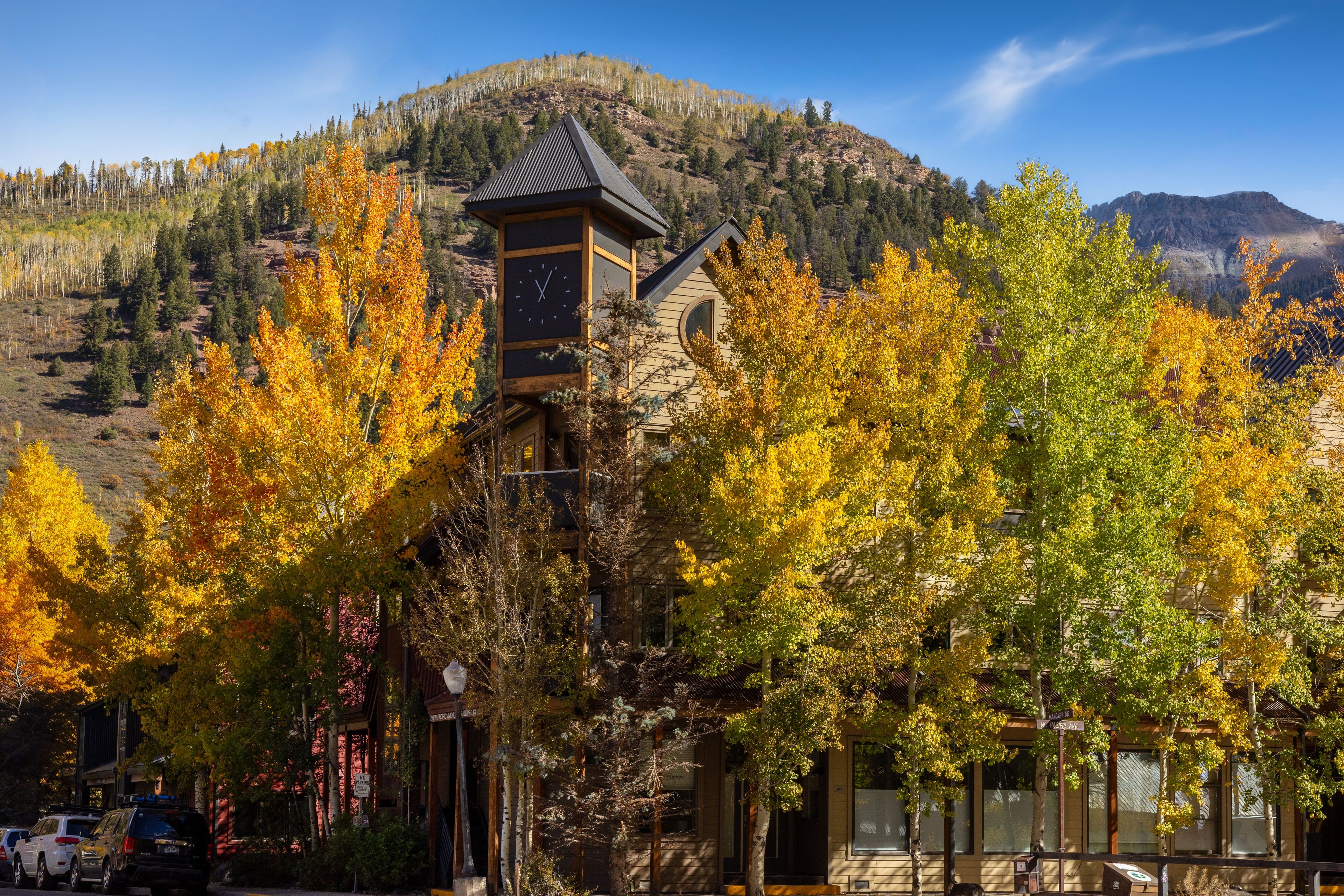 A mountain lodge with a prominent clock tower, surrounded by autumn foliage.