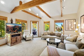 A living room with a television, sofas, a coffee table, and large windows with views of trees and mountains. - Lulu City #4C Fresh Mountain Style Steps to Coonskin Lift Sleeps 7 (Telluride)