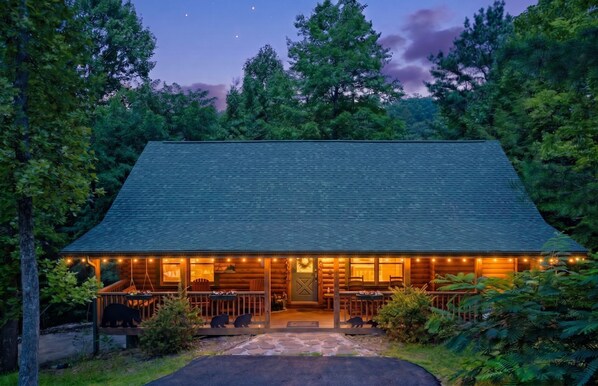 Une cabane en rondins avec un porche, une porte d’entrée et un petit jardin devant.