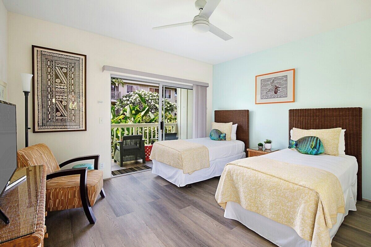 Habitación de hotel con dos camas, una silla, ventilador de techo y balcón con plantas.