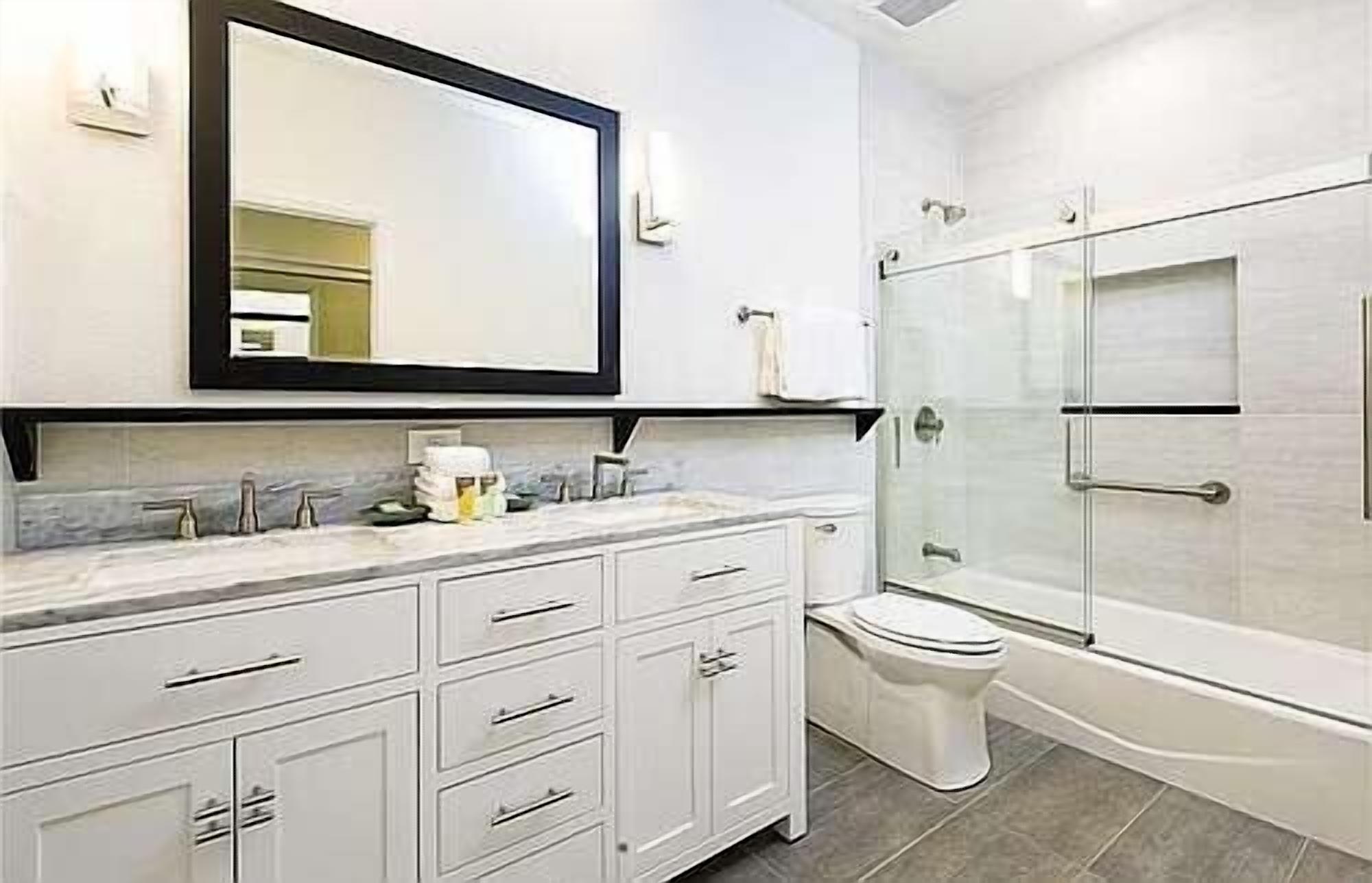 A modern bathroom with a white vanity, a large mirror, a toilet, and a glass-enclosed shower.