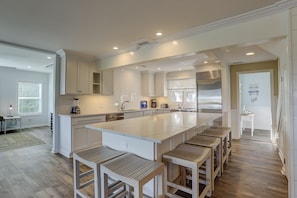 A modern kitchen with a large island, white cabinetry, and a wooden floor.