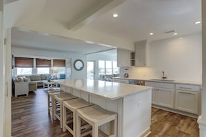 A modern kitchen with a central island, wooden stools, and a dining area with a sofa and table.