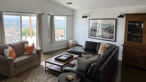 Ein geräumiges Wohnzimmer mit großem Fenster, Deckenventilator, Holzschrank und einem gerahmten Landschaftsbild.