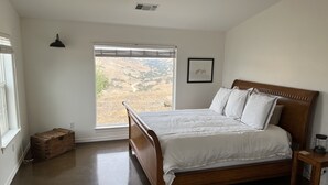 Ein Schlafzimmer mit einem hölzernen Bett, einem Fenster mit Landschaftsblick, einem kleinen Nachttisch und einer Wandleuchte.