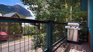 Un balcon avec un barbecue, une vue sur une montagne et une rue bordée de voitures garées.