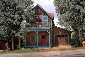 A two-story wooden house with a red door and a balcony.