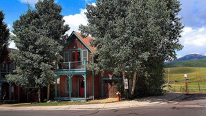 Un bâtiment en bois à deux étages, avec une porte rouge et un balcon, entouré d’arbres.