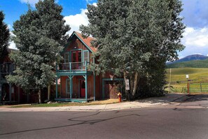 A two-story wooden building with a red door and a balcony, surrounded by trees.