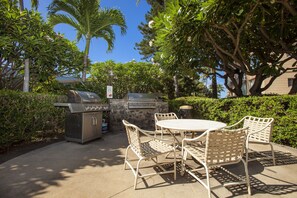 Une terrasse extérieure avec un barbecue, des chaises en osier blanc et une table ronde.