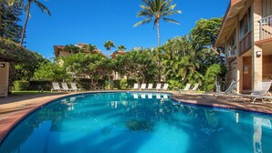 Una piscina cristallina blu circondata da sdraio e palme, con edifici sullo sfondo.