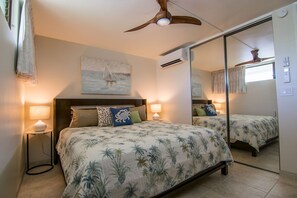 A bedroom with a bed, two bedside lamps, a ceiling fan, a painting, and a large mirror. - Custom remodel and breathtaking views (Lahaina)