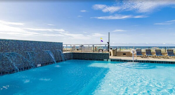 A swimming pool with a tiled edge, a flag, and lounge chairs. - Phoenix X 1109 | Next to Flora-Bama! | Beachfront | Pools | My Beach Getaways (Orange Beach)