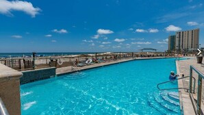 Una piscina con agua azul cristalina, sillas de descanso y vistas al océano y un edificio de hotel al fondo.