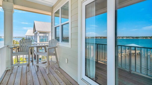 A covered deck with a view of the ocean, wooden chairs, and a table. - Good Time Charlie by GSVR | Lagoonfront Home w/ Pool, Firepit & Beach Access + FREE Activities/Golf (GULF SHORES)