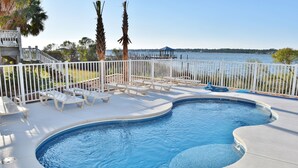 A swimming pool with a curved edge, surrounded by white deck chairs and a white fence. - Good Time Charlie by GSVR | Lagoonfront Home w/ Pool, Firepit & Beach Access + FREE Activities/Golf (GULF SHORES)