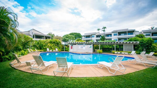A swimming pool with lounge chairs, surrounded by greenery and modern buildings.