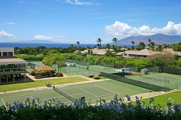 Una cancha de tenis con vista a una montaña y un edificio con una zona de estar techada.