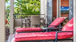 Un espace extérieur aménagé, abrité et doté de chaises en osier et de fauteuils confortables avec des coussins rouges, offrant une vue sur un jardin luxuriant et un paysage pittoresque.