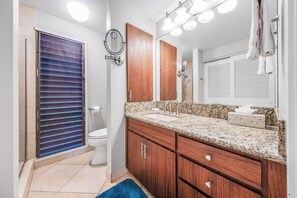 A bathroom with a toilet, a sink with a granite countertop, wooden cabinets, a mirror, and a towel hanging on the wall. - Wailea Ekolu #501 Panoramic Ocean View, Ground Floor, Wifi, A/C, Near Beach (Wailea)