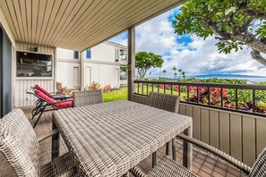A covered outdoor seating area with wicker furniture, a view of the ocean, and a building with white siding. - Wailea Ekolu #501 Panoramic Ocean View, Ground Floor, Wifi, A/C, Near Beach (Wailea)